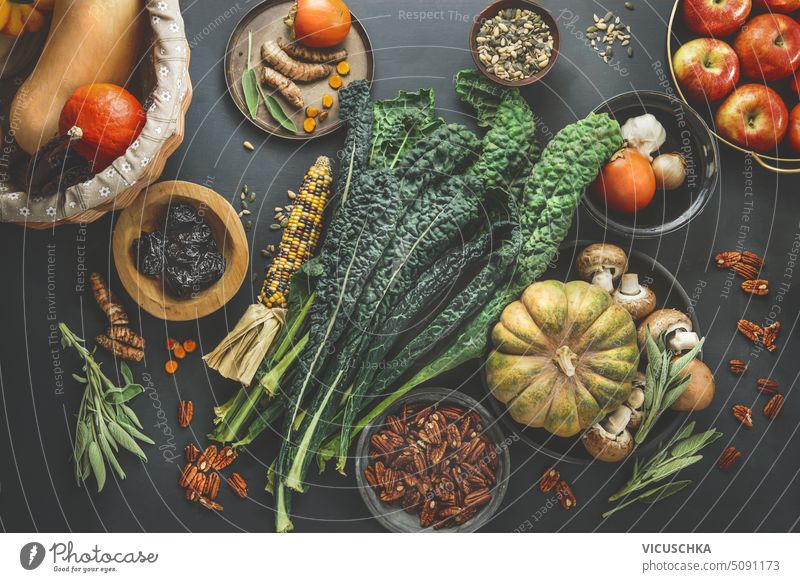 Healthy seasonal vegan ingredients: kale, pumpkin, corn, apples, pecan nuts and seeds selection with fresh herbs and spices on rustic kitchen table, top view
