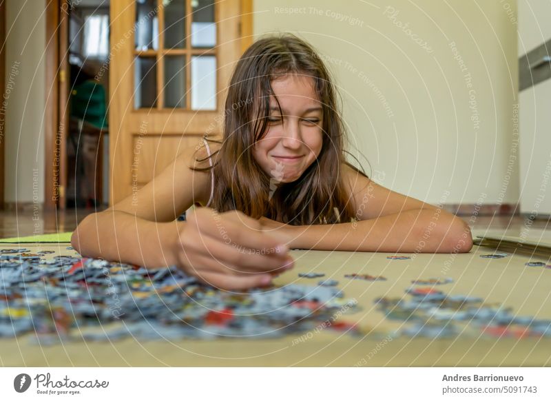 Teenage brunette girl doing puzzle lying on the floor of her house, she spends time running away from technology and enjoying traditional games. background