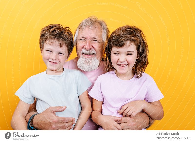 Happy grandfather with grandchildren on yellow background man embrace hug laugh love close bonding relationship happy enjoy smile cheerful positive senior