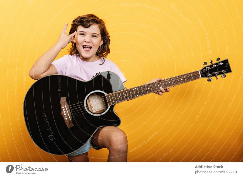 Cheerful girl with guitar showing rock gesture horn sign rock and roll play acoustic happy excited cheerful kid child entertain sound energy audio song talent