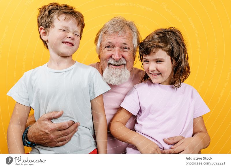 Happy grandfather with grandchildren on yellow background man embrace hug laugh love close bonding relationship happy enjoy smile cheerful positive senior