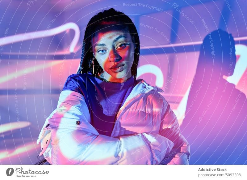 Trendy African American woman looking at camera in illuminated studio confident style self assured glow neon model gorgeous charismatic millennial appearance