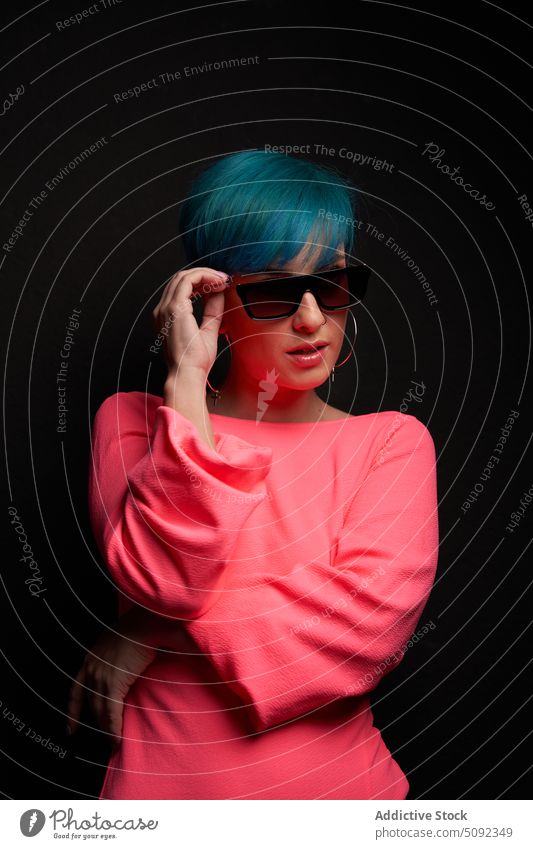 Modern woman adjusting sunglasses in studio style trendy model cool confident individuality modern hipster highlight blue hair short hair outfit appearance