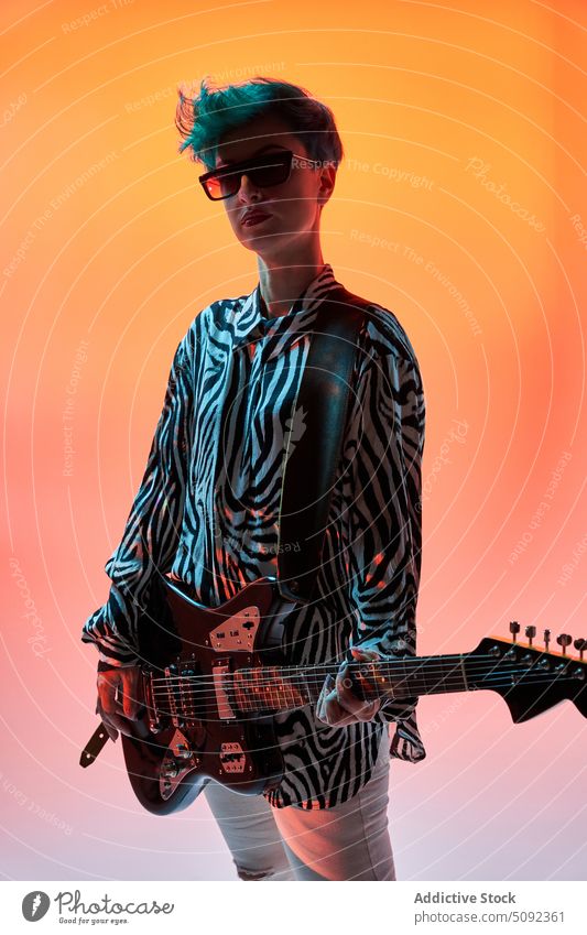 Stylish woman playing guitar in colorful studio electric music style musician guitarist trendy hipster fashion outfit sunglasses instrument melody sound female