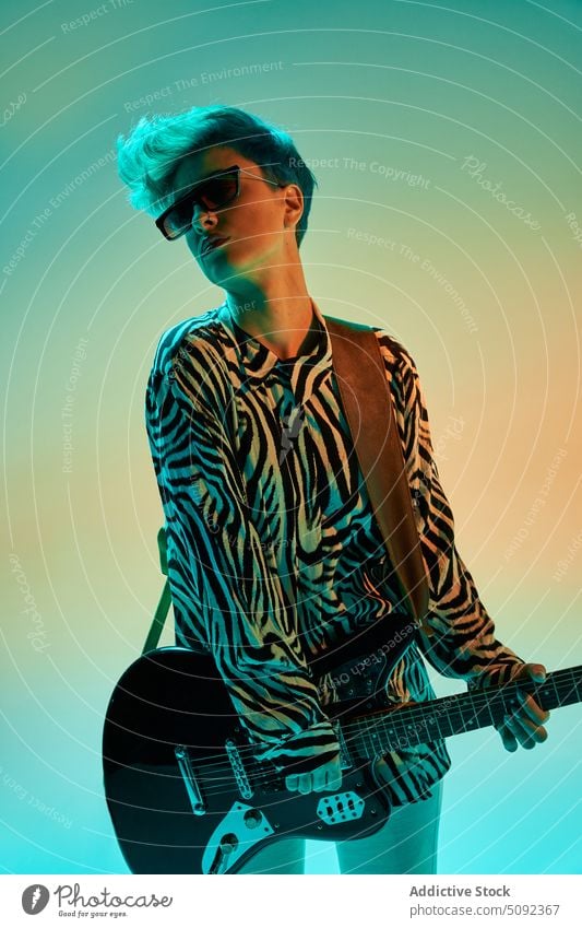 Stylish woman playing guitar in colorful studio electric music style musician guitarist trendy hipster fashion outfit sunglasses instrument melody sound female