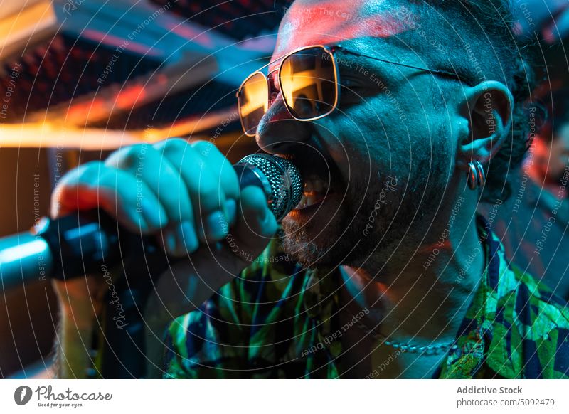 Man in sunglasses singing into microphone in studio man vocalist song singer voice perform rehearsal talent music energy modern musician record practice sound