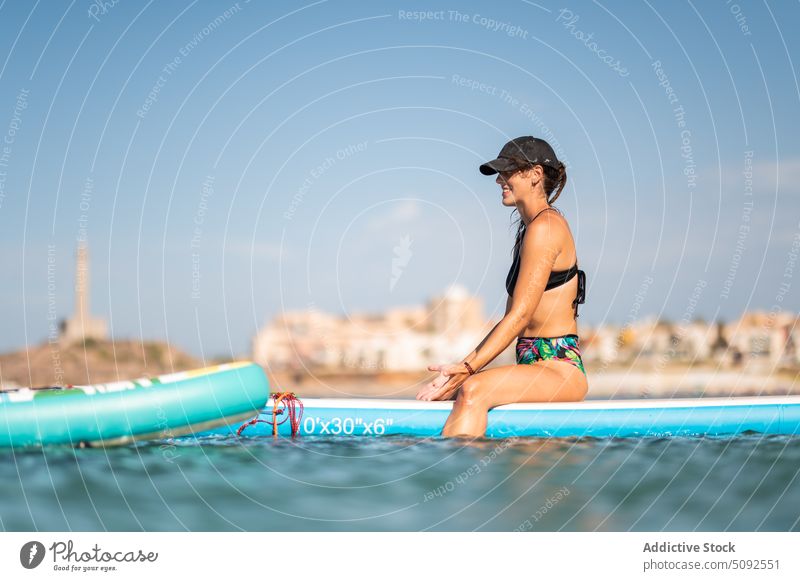 Fit woman sitting on paddleboard stretch smile sup board sea fit glad sport healthy activity summer recreation blur water happy delight active nature wellness