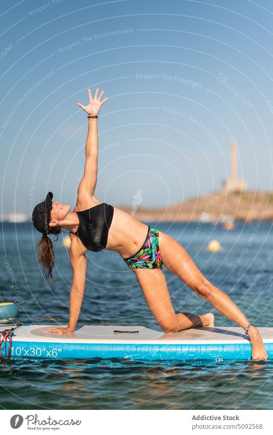 Fit woman doing yoga on paddleboard balance sup board sea water healthy exercise activity practice side plank on the knee swimwear recreation summer harmony