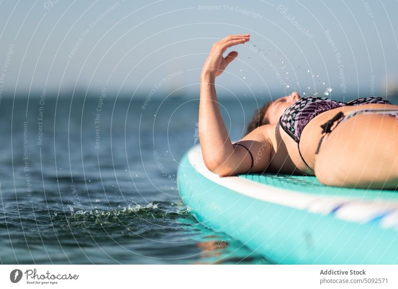 Woman relaxing on paddleboard in sea water woman suntan sup board chill rest float calm lying vacation summer sunbath bikini summertime carefree idyllic