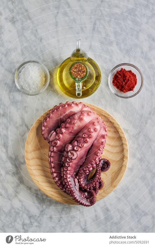 Octopus on wooden plate with seasonings and oil octopus mediterranean tentacle uncooked dish food kitchen paprika round seafood portion product ingredient