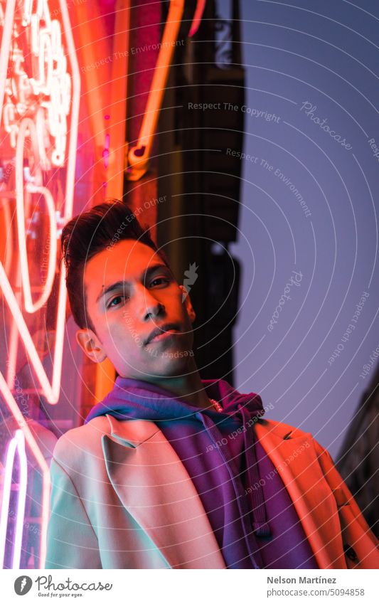 Portrait of young hispanic man with red neon light on the face, wearing a beige blazer street bright fashion suit party look leather night guy concept colourful