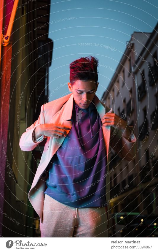 Portrait of young hispanic man with red neon light, wearing a beige blazer and a purple hoodie street bright fashion suit party look leather night guy concept