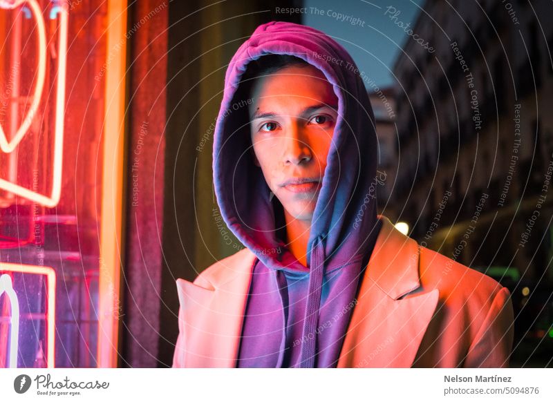 Young millennial hispanic man with red neon light reflection and a hood young street bright fashion suit look leather night guy concept colourful fashionable