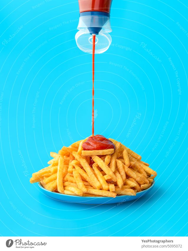 Pouring ketchup sauce over french fries, isolated on a blue background abundance bright calories color concept copy space crispy cuisine cut out deep-fried