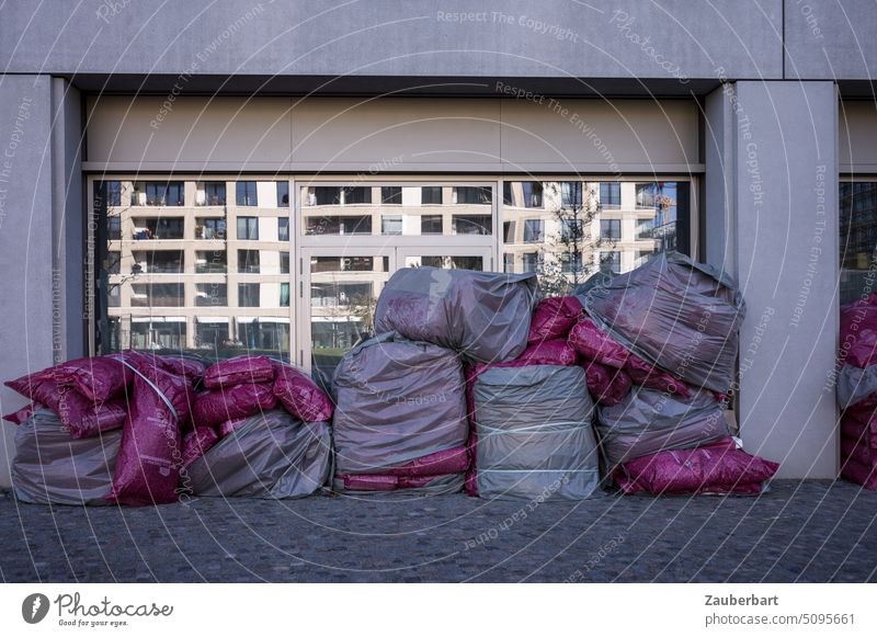Garbage bags pile up in front of a window in which a modern residential building is reflected Trash refuse sacks Slice mirror reflection Facade
