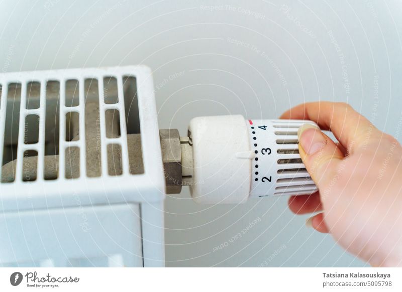 A hand turns the regulator on the heating radiator of the house. The concept of saving resources and heat energy in connection with the energy crisis turn on