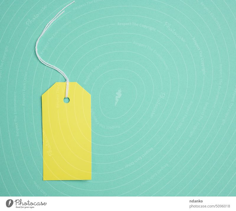 Empty yellow cardboard tag on a white rope, green background. Price tag template paper label string sale blank price retail empty gift sell hang pricing buy