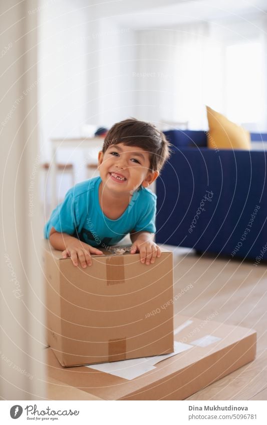 4 or 5 year old boy playing with boxes after moving to new home with his family. Joy of moving to a new apartment. Smiling kid holding a carton box.