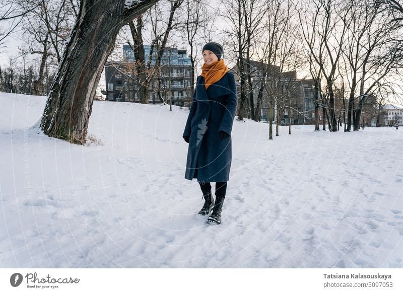 A woman walks on the snow-covered ground and smiles winter cold happiness happy joy female people person adult coat cheerful alone toothy smile real life