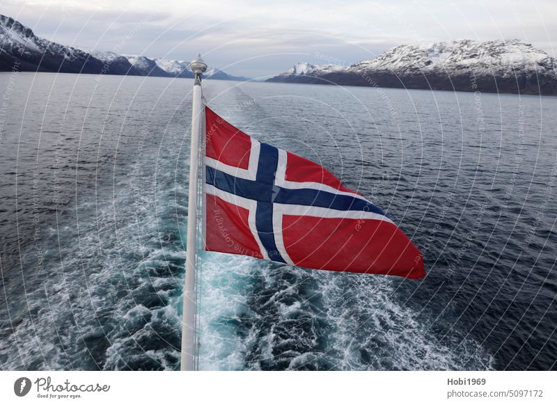 View from a ship into a fjord near Alta in Norway with a flag in the foreground. Flag boat Stern Current Fjord mountain mountains Snow Water Sea water Ocean