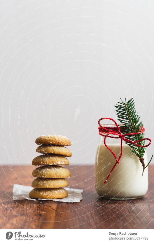 A glass of milk with a fir branch and red bow and stacked cookies on a wooden table. Christmas. Milk Glass Christmas & Advent Cookie baked cute Delicious