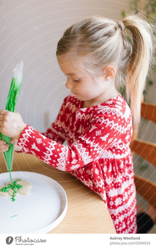 Little girl decorating a Christmas cookie with green frosting bake baking beauty celebration child childhood children christmas christmas tree closeup