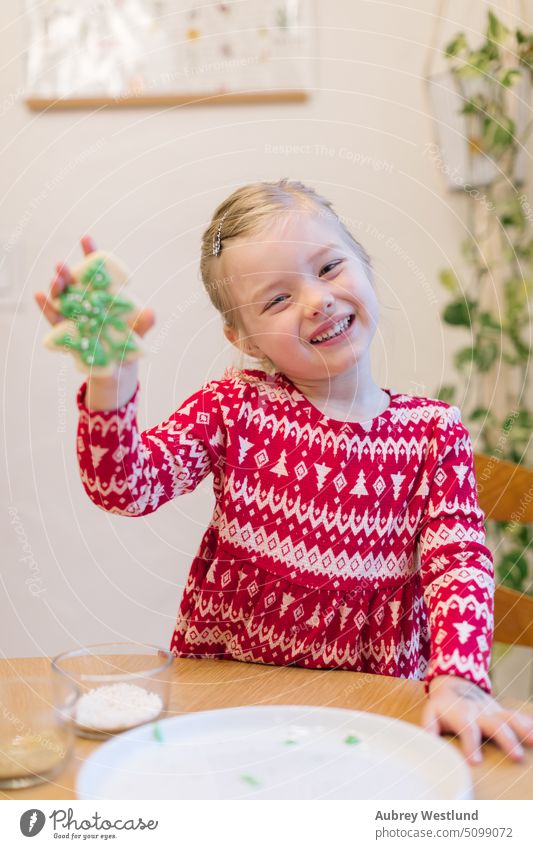 Smiling little girl in red Christmas sweater showing off her Christmas tree cookie bake baking beauty celebration child childhood children christmas