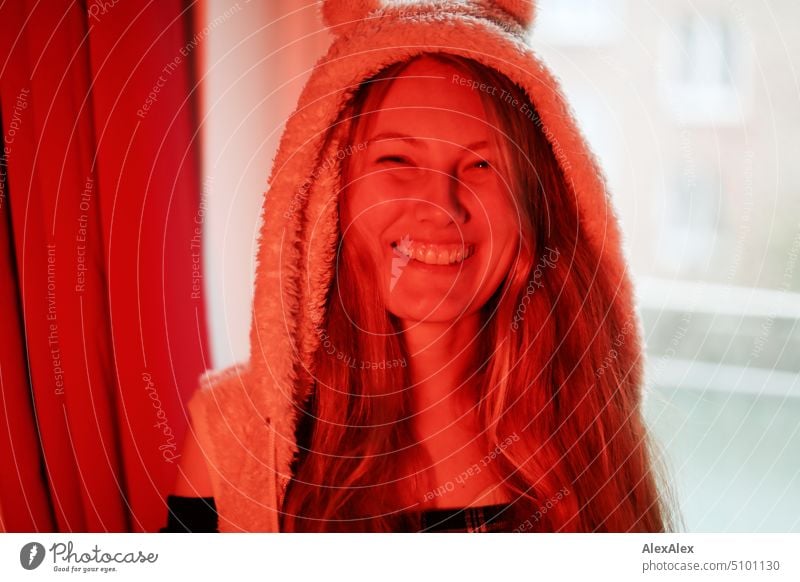 Close portrait of young blonde woman smiling standing at window illuminated with red light Woman Young woman Blonde Long-haired Smiling Joy Window Slim kind