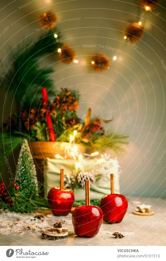 Christmas red apples with cinnamon sticks on table with Christmas tree, gift box and bokeh. Front view christmas christmas tree front view festive green fir