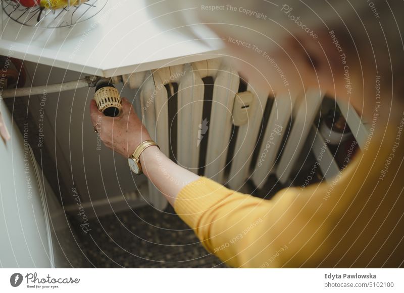 Woman adjusting the temperature of a radiator at home people woman senior mature female elderly house old domestic life pensioner retired real people adult
