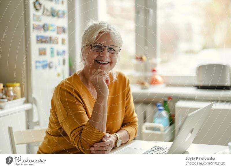 Mature woman working on laptop in kitchen smiling happy enjoying positive people senior mature female elderly home house old aging domestic life grandmother
