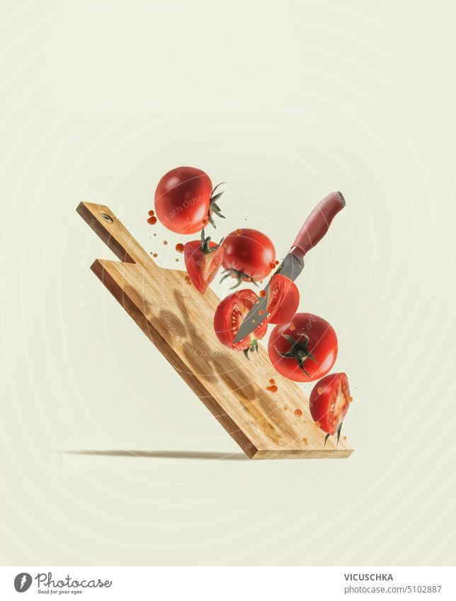 Flying sliced tomatoes, knife and wooden cutting board at pale beige background. Levitation ingredients with fresh vegetables. Creative food concept. Front view.