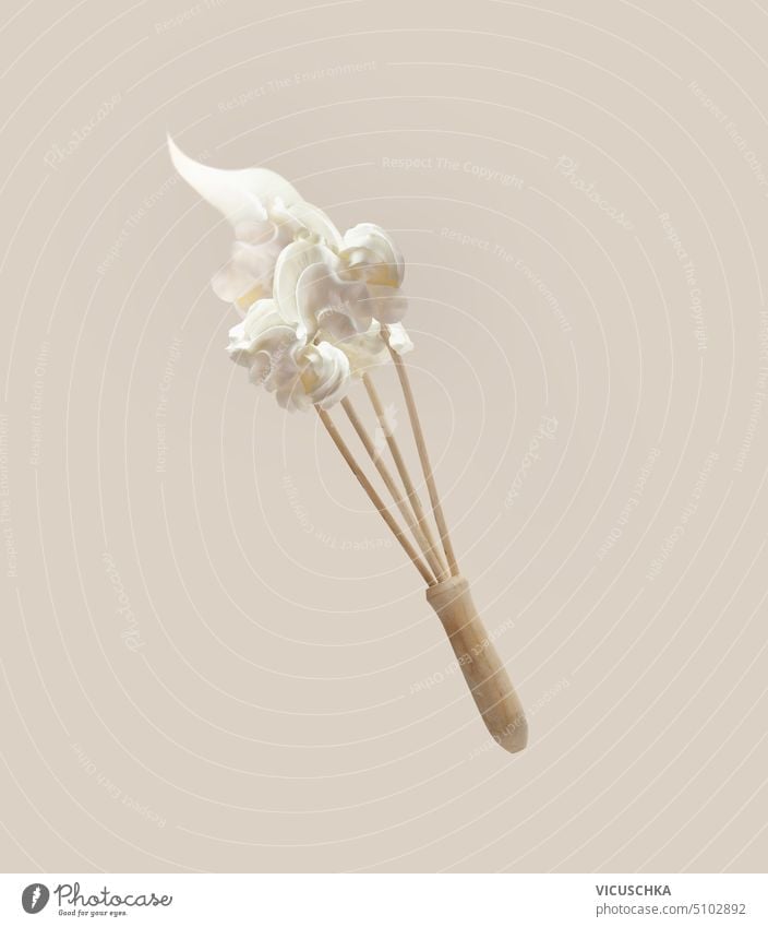 Whipped cream at flying wooden whisker at pale beige background. Levitation food concept with baking utensils. Front view. whipped cream levitation front view