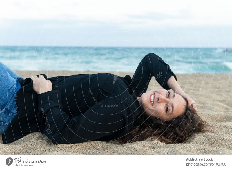 Cheerful woman lying on sand beach joy coast leisure chill having fun cheerful smile sea happy positive female young relax rest curly hair casual weekend