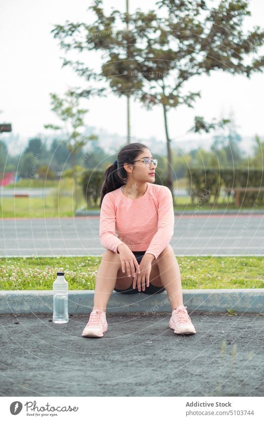 Sportswoman sitting on curb with bottle of water sportswoman break rest runner leisure healthy physical wellbeing fit athlete plastic daytime vitality
