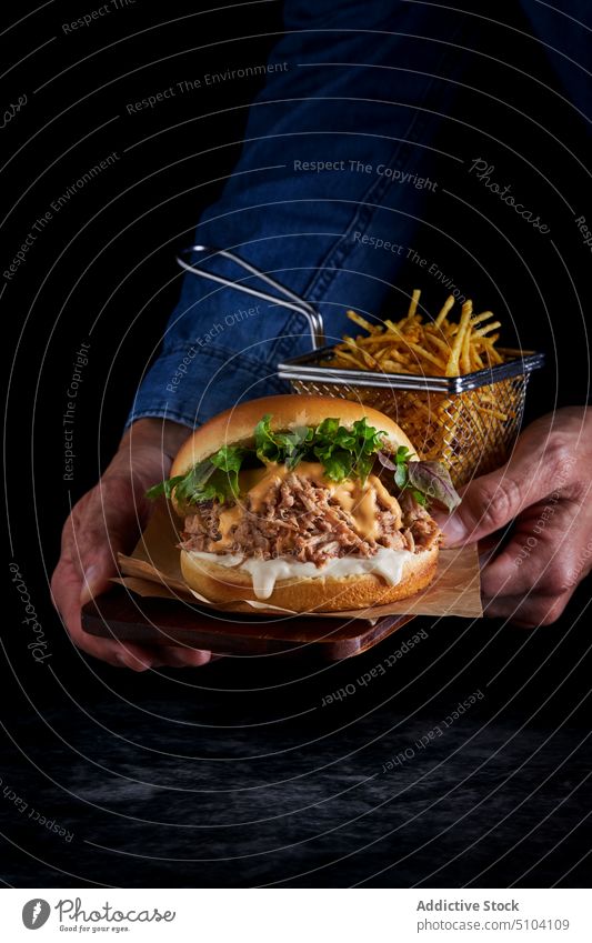 Crop person with delicious burger hand fast food junk food french fries culinary meal unhealthy calorie lettuce pork bun meat flavor palatable taste ingredient