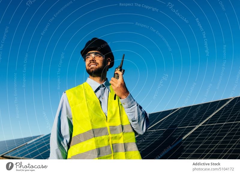 Worker with walkie talkie near solar panels in daylight man handheld radio report control technician photovoltaic renewal sustainable battery alternative
