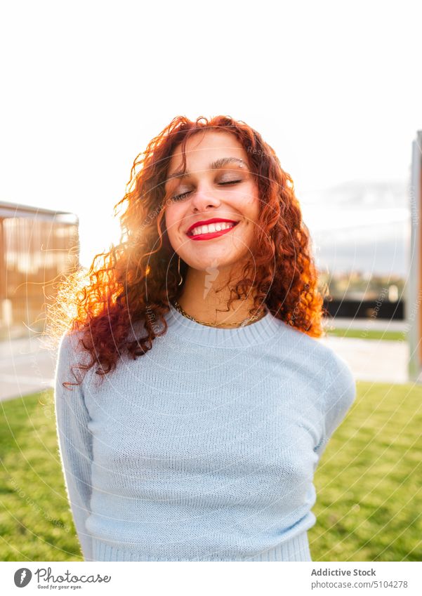 Happy young woman near lawn smile happy sunrise street curly hair red hair morning early female sweater cheerful redhead casual positive summer carefree daytime