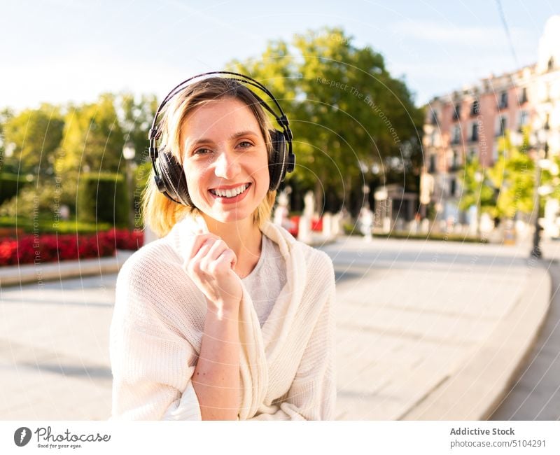 Positive woman smiling while listening to favorite song in headphones on street music park smile city happy meloman portrait cheerful positive female young