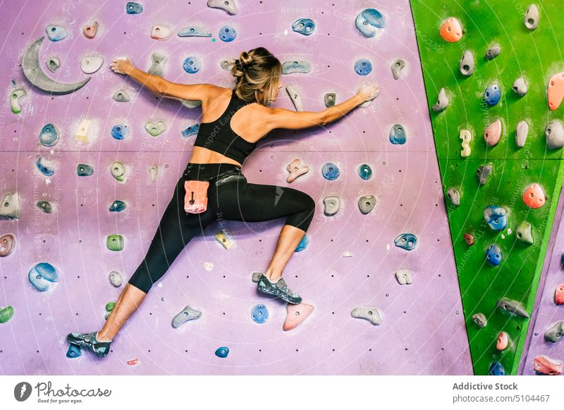 Female climber hanging on wall sportswoman training gym grip practice female power bouldering extreme activity effort energy strong hobby athlete workout