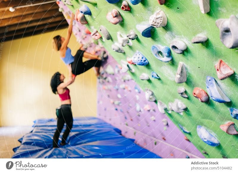 Sportswoman climbing wall with help of trainer sportswomen climber support together training female coach effort instructor workout gym exercise athlete strong