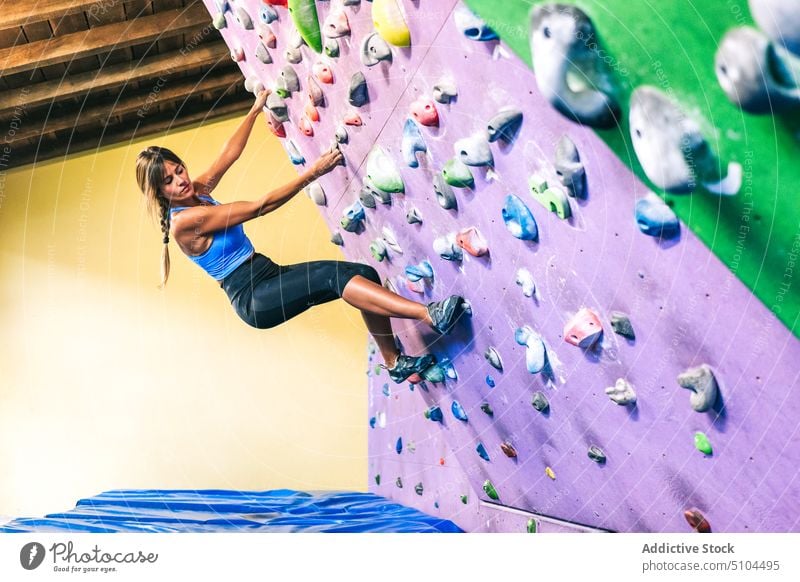 Female climber hanging on tilted wall sportswoman training gym grip practice female mat power bouldering extreme activity effort energy strong hobby athlete