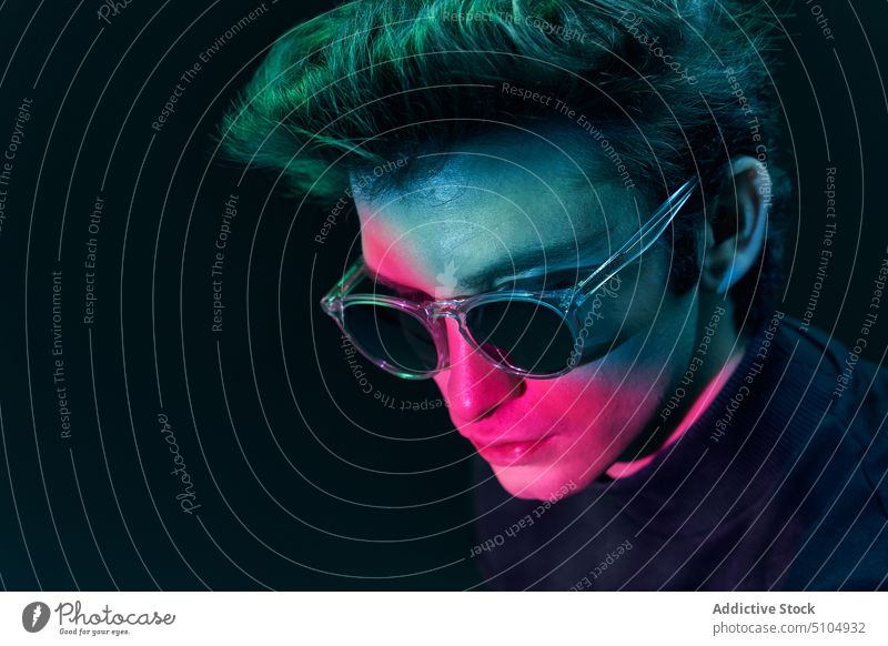 Young male model in sunglasses standing in studio man neon light studio shot dark individuality emotionless portrait unemotional young luminous contemporary