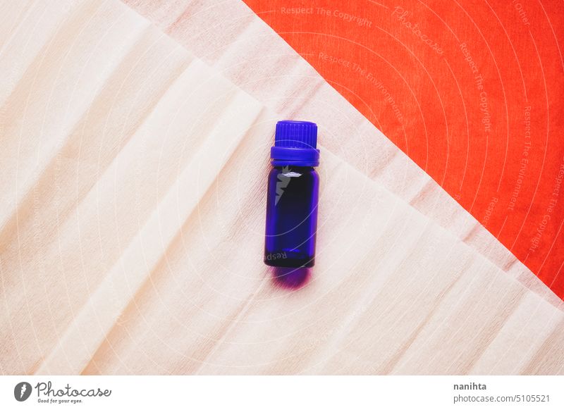 Flat lay background image of a dark blue bottle of essential oil against paper background cosmetics organic minimal minimalistic texture orange red coral peach