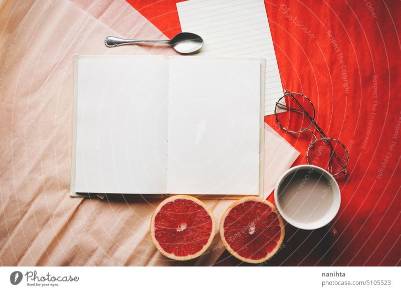 Colorful flat lay of an open diary surrounded by common objetcs as a work space mockup book page background blank white orange red grapefruit glasses notebook