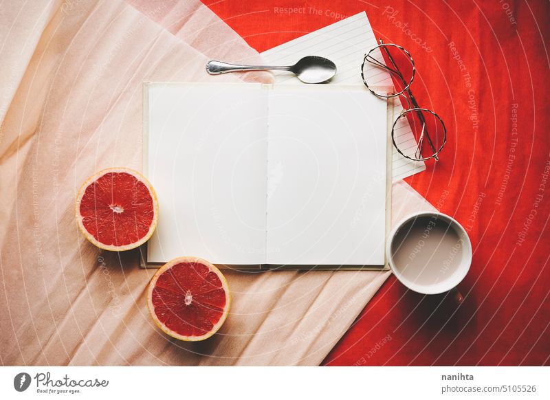 Colorful flat lay of an open diary surrounded by common objetcs as a work space mockup book page background blank white orange red grapefruit glasses notebook