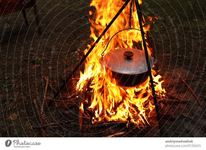 Cooking outdoors in field conditions. Cauldron on a fire in the forest. Cooking at the stake while traveling. Tripod with a bowler hat on a fire on picnic. Conceptual travel, trekking and adventure