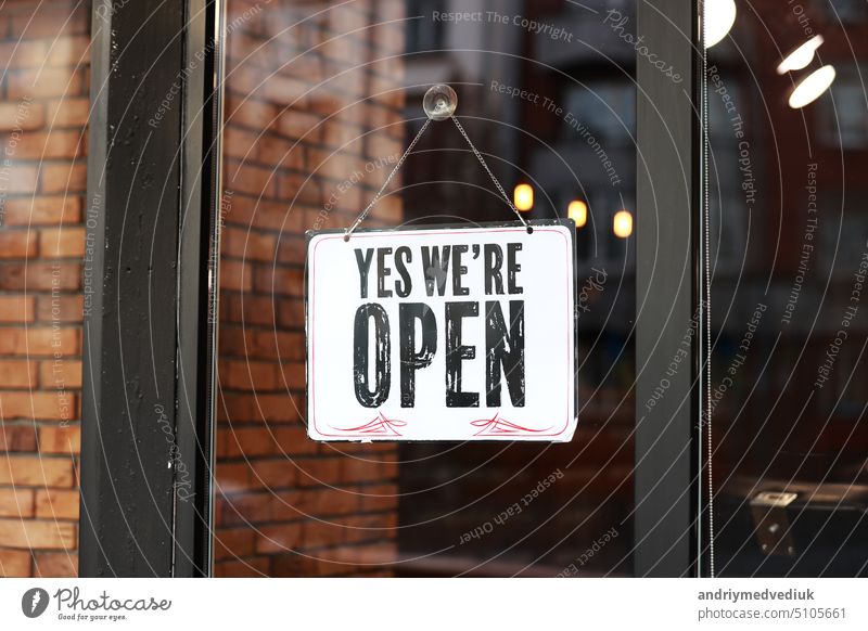 Inscription Yes we're open metal plate with black and white sign on glass door store, cafe, beautystore, barbershop after coronavirus lockdown quarantine. business reopen again