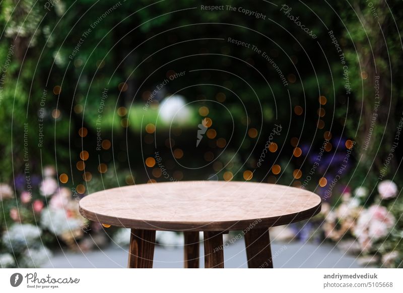 Round wooden table on a green nature with light bulbs background. Outdoor table at desk. Grass, greens and party decoration bushes in the background. circle