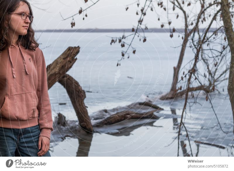 A young girl stands pensively by the lake, whose surface is covered with thin ice Girl Young woman Lake Water Surface Winter Ice Cold icily chill Meditative